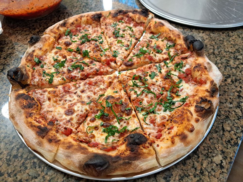 NY style pizza cut into slices on a tray. Most of the slices are sprinkled with fresh basil.