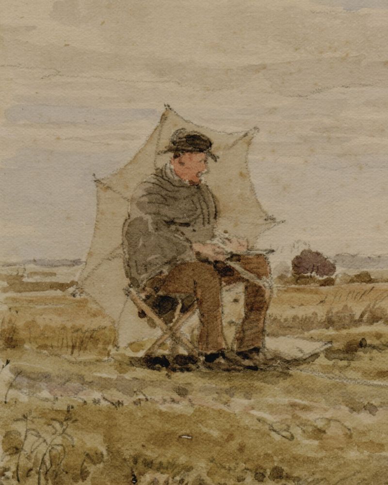 A man is holding an umbrella while sat on a fold out chair in the countryside. He is wearing a brown brimmed hat, grey shawl, and brown trousers and shoes. 