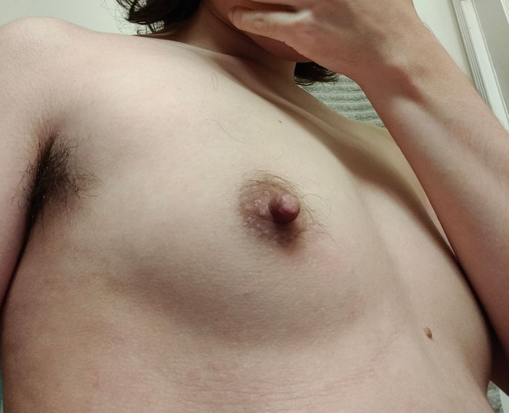 a white trans man showing off his pre-op chest. only a light shadow beneath indicates the curve of his small breast. one nipple is swollen with arousal, and the other is covered by his forearm.