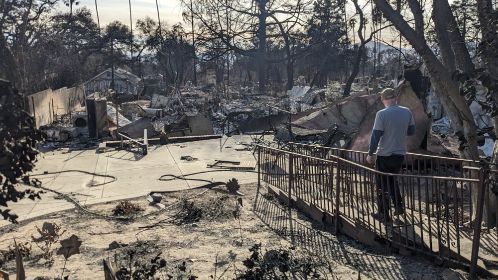A man walking toward the burned wreckage of his former home