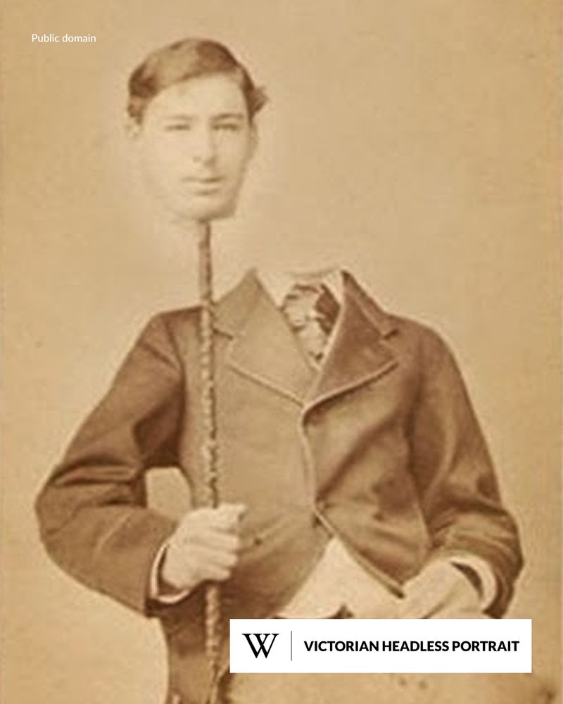 A young man in Victorian attire poses with his head seemingly detached and held aloft by a stick.