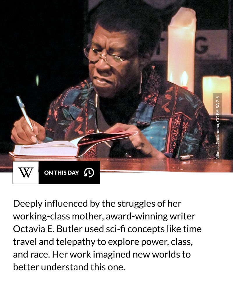 A person wearing glasses and a patterned shirt signs a book with a pen, seated at a table with large lit candles in the background. Text says: Deeply influenced by the struggles of her working-class mother, award-winning writer Octavia E. Butler used sci-fi concepts like time travel and telepathy to explore power, class, and race. Her work imagined new worlds to better understand this one.