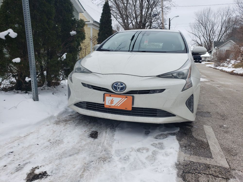 A Toyota Prius parked on a snowy street, with an orange and white avali flag front vanity plate
