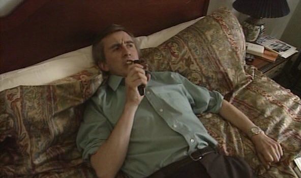 Alan Partridge lying on his back on a bed, speaking into a dictaphone