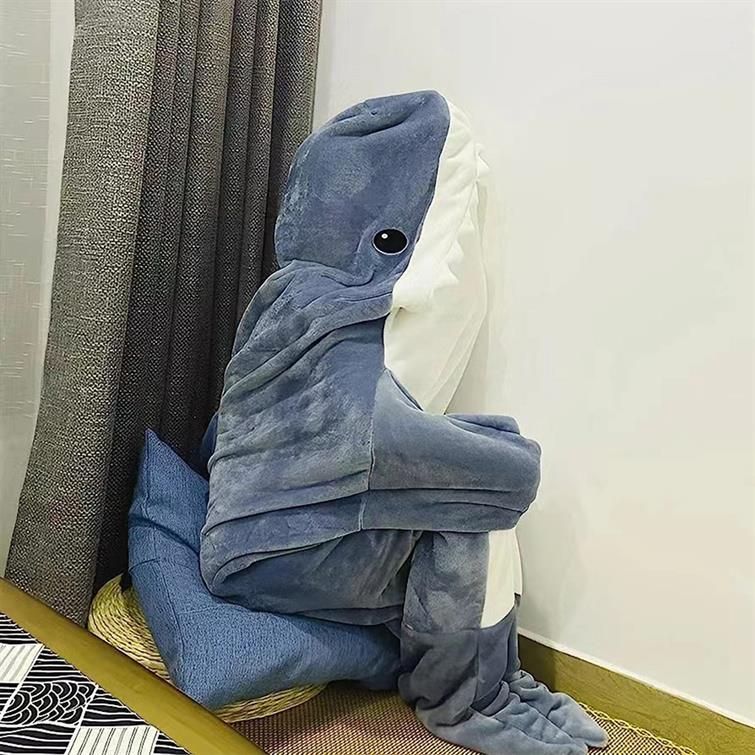 A person in a very loose shark "costume" huddled in a corner sitting on a pillow.