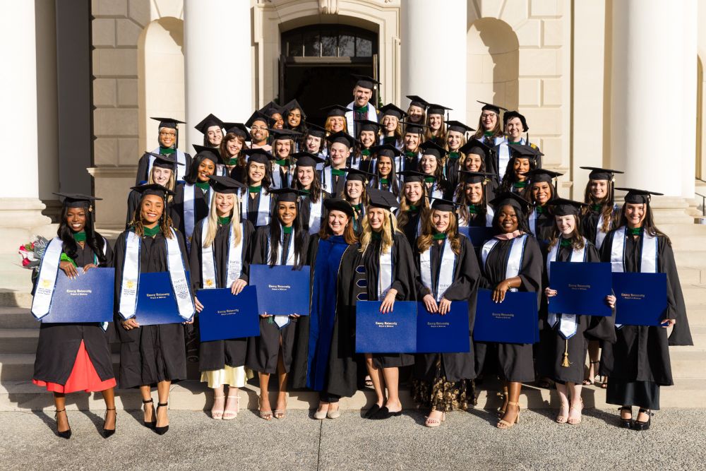 Group photo of the Class of 2024 Emory Physician Assistant Program graduates in their caps and gowns holding blue diploma covers