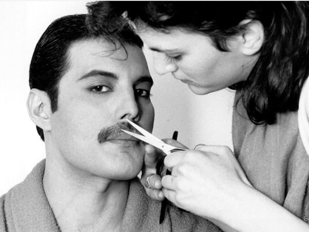 A woman is holding a pair of hairdressing scissors in the direction of a man's moustache.