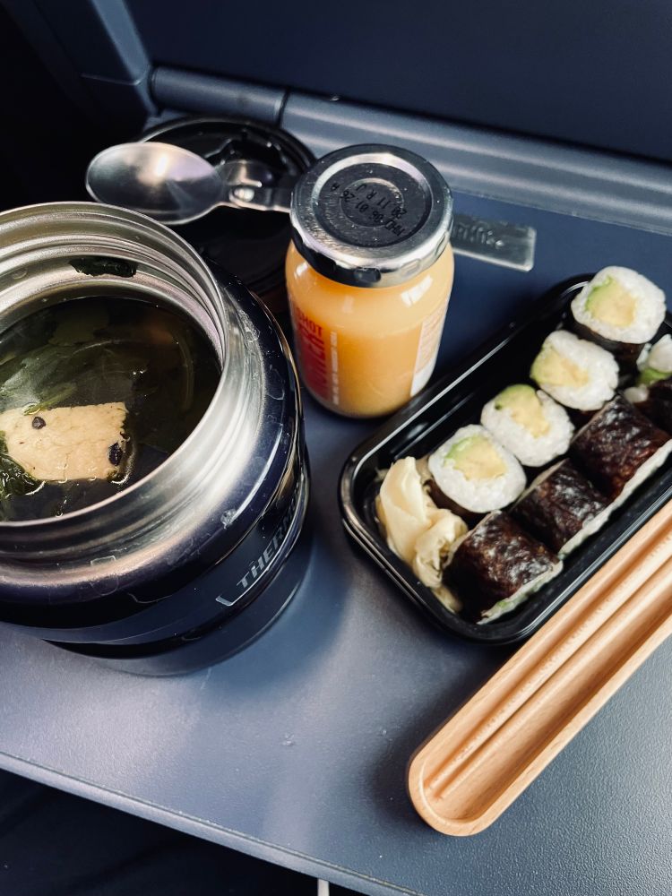 thermos with soup, some sushi on a small tray, chopsticks in a wooden travel case, a small jar of ginger juice