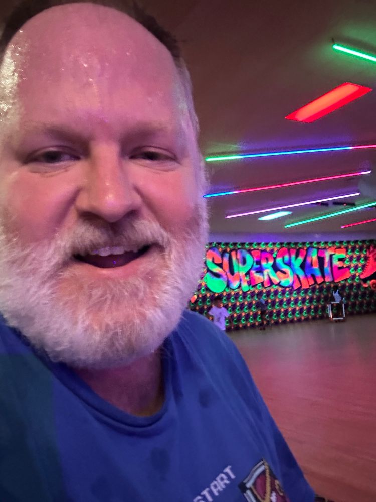 Photo of a very sweaty bearded me at a roller rink with some solid glow paint in the background.  