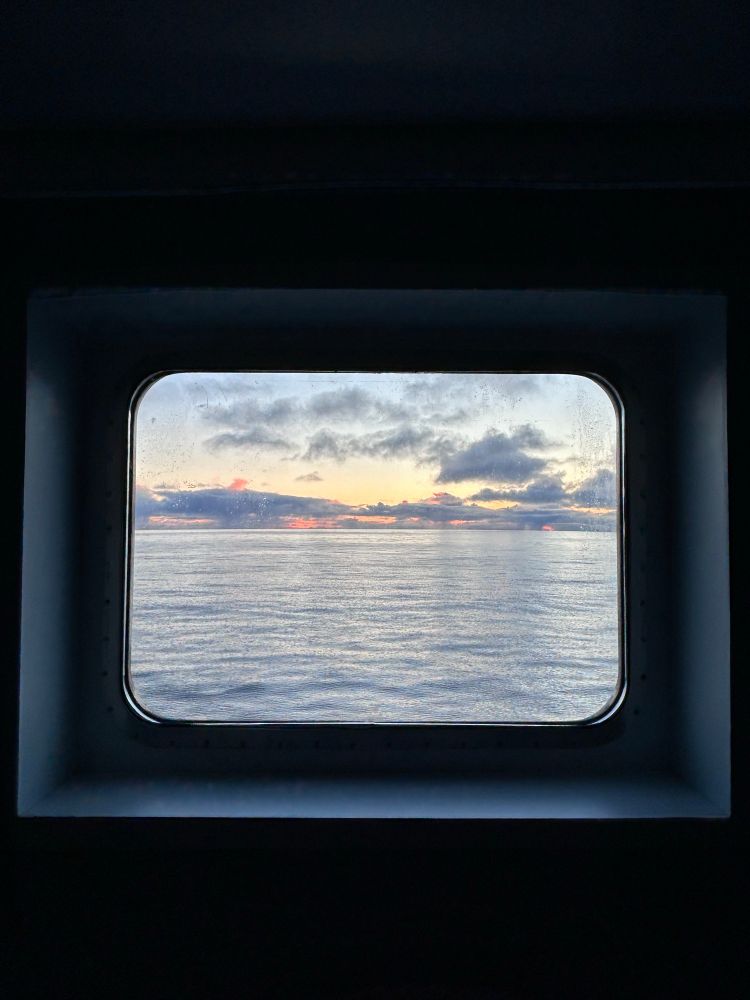 The sea viewed through a window. The sun has just moved out of sight but you can still see a warm glow behind the clouds. 