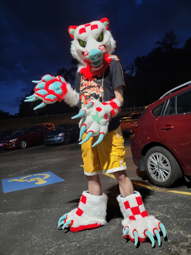 A red and white picnic themed bear full partial fursuiter standing in a parking lot at night