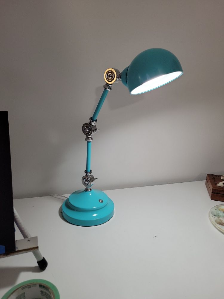 A ridiculously cute turquoise desk lamp shines brightly on an art table.