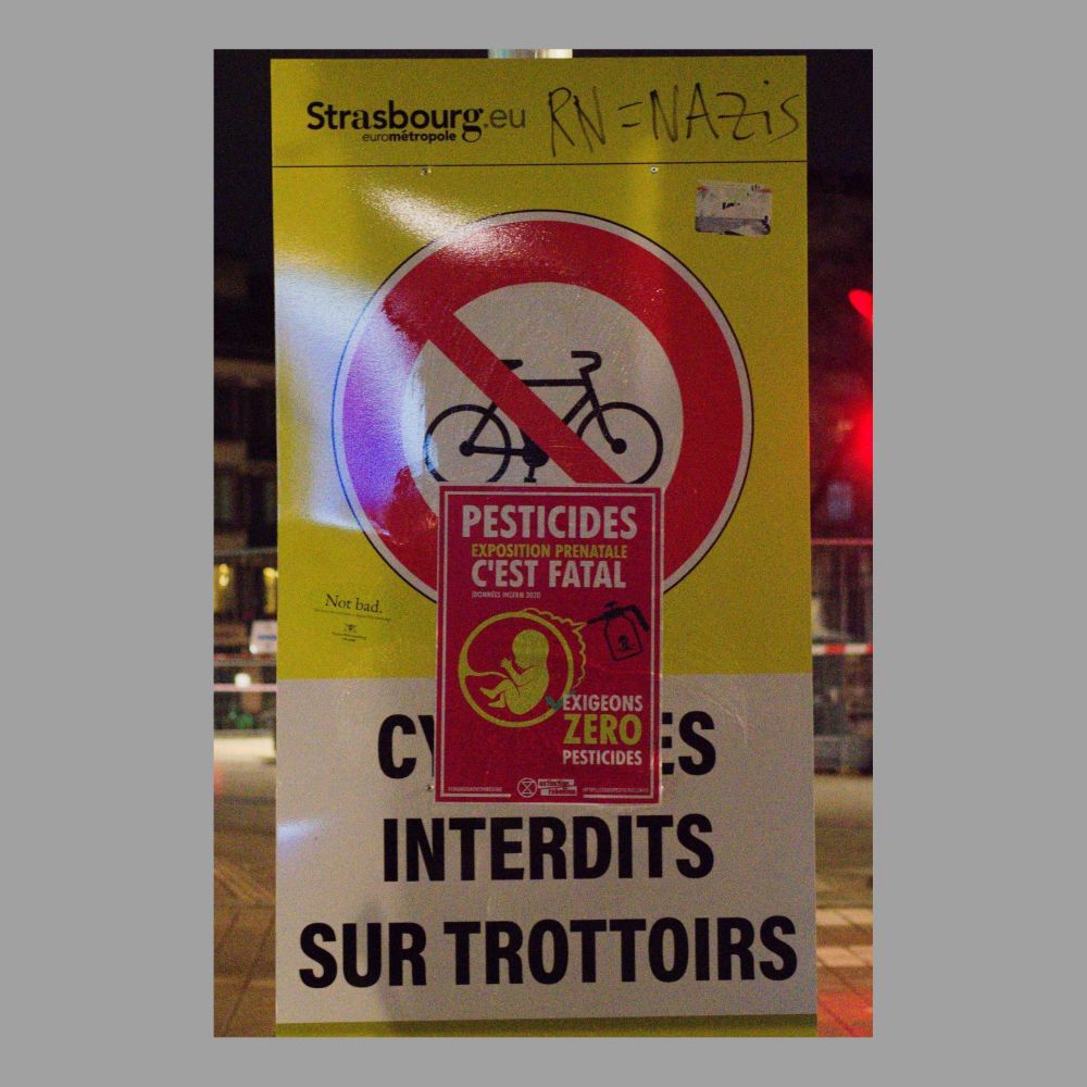 Photo d'un panneau publicitaire avec une affiche de la campagne XR Changement de régime. On peut notamment y lire "Pesticides interditssur le trottoir".