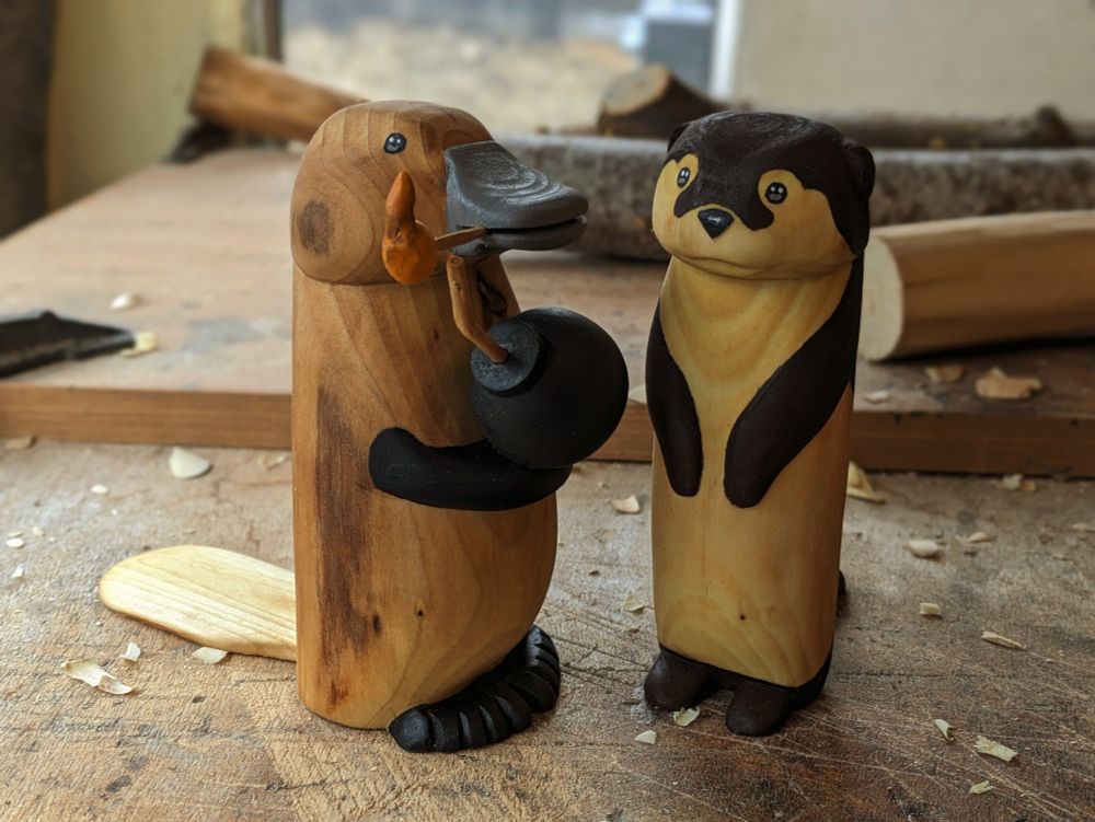 Wood sculpture of a platypus holding a bomb ready to light the fuse and a standing otter