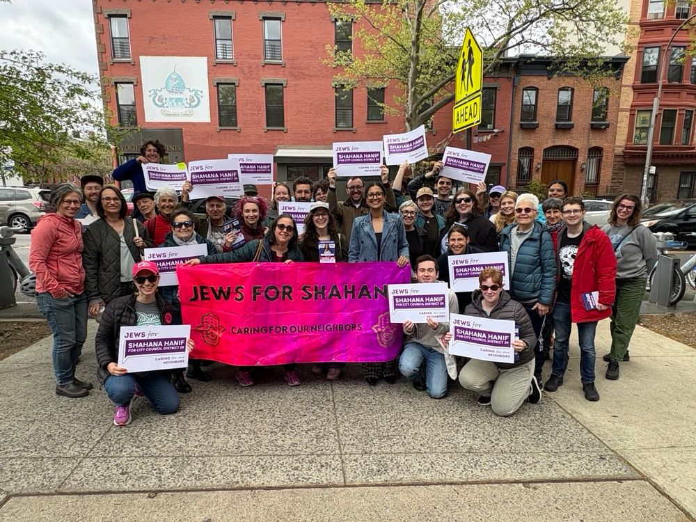 40 people including Shahana Hanif behind a big vibrant pink and purple banner saying Jews For Shahana, Caring for our neighbors and holding Jews for Shahana signs! 