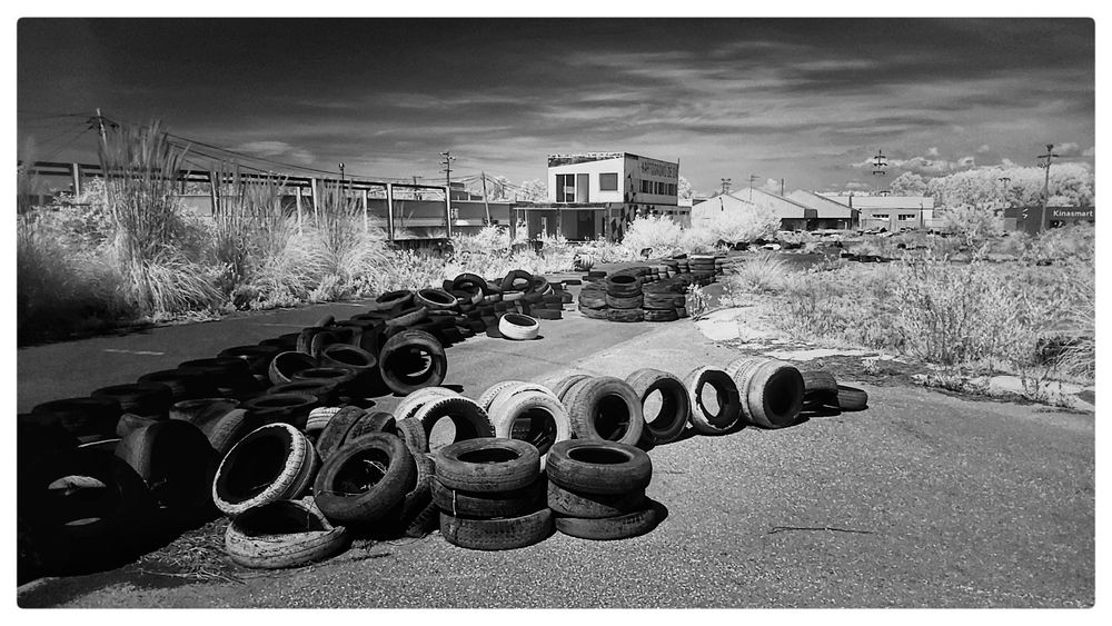 Infrared image of the abandoned Kartódromo track in Oiã, Portugal. In the foreground are rows of old tyres marking the track, while in the background is scrub vegetation and the old buildings of the Kartódromo. Taken with a Samsung A70 smartphone and a 720nm infrared filter.