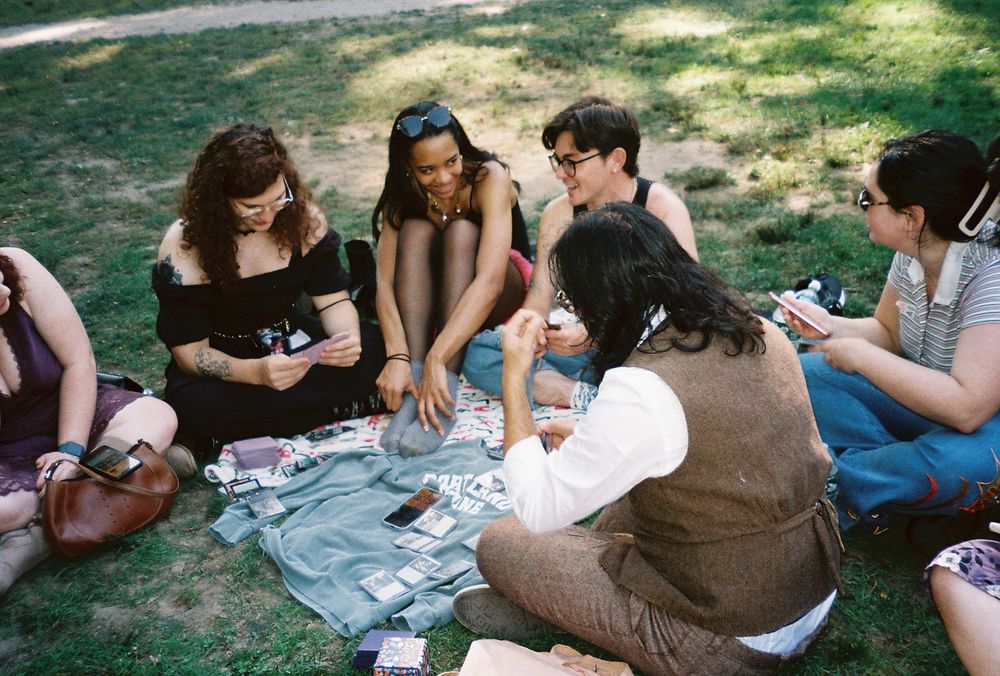 a film photograph of alex and friends chatting and laughing while playing magic the gathering on a blanket in central park