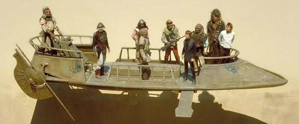 A still from Star Wars: The Return of the Jedi showing the heroes standing in a cargo skiff just before the battle above the Sarlacc pit.