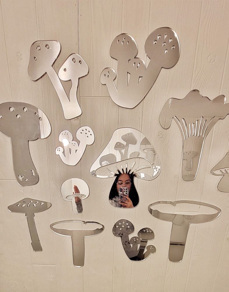 Woman posing in the reflection of a mushroom shaped mirror that is surrounded by different types of mushroom shaped mirror.
