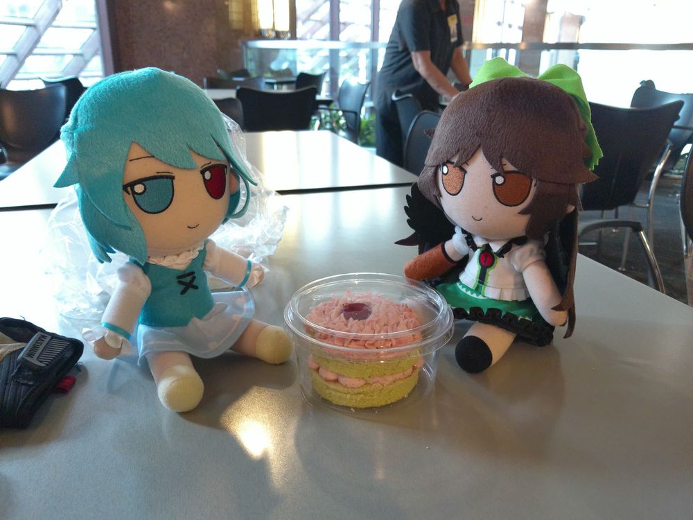 Fumo plushies of Kogasa Tatara and Utsuho Reiuji sitting next to a smol cake