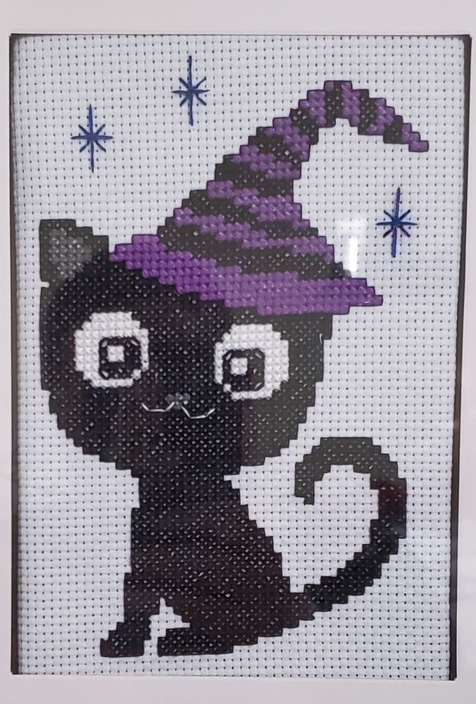 Cross stitch of a black cat in a purple and black hat