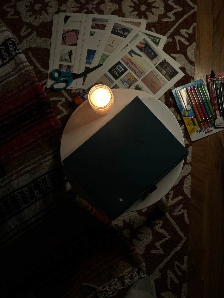 a photo of the floor showing part of my rug with my blanket put down and my vision board cards, scissors, ink pens a candle and my journal on top of a stool.