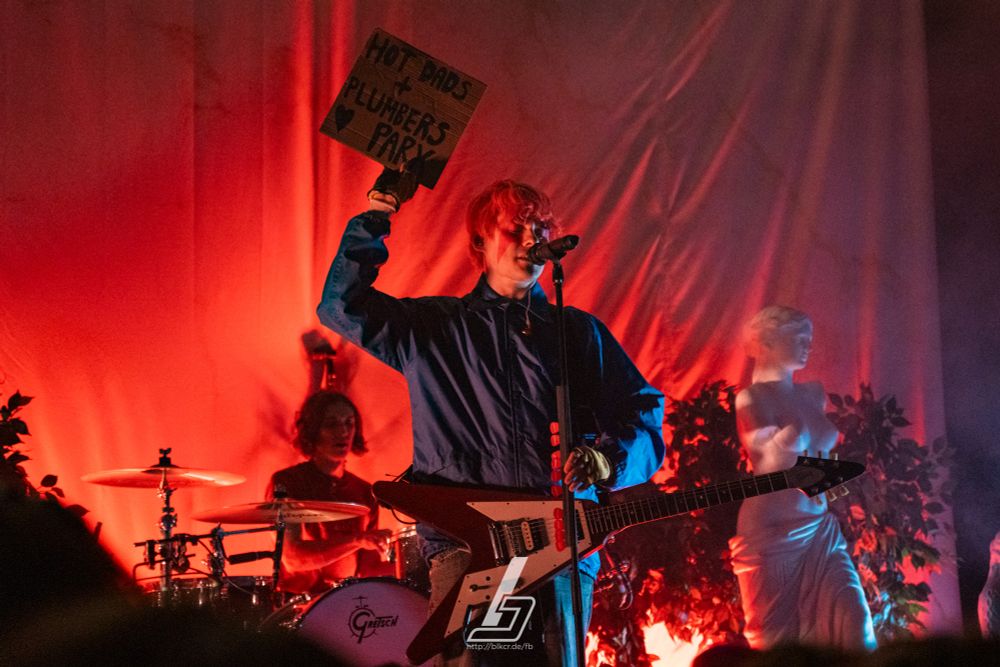 Awsten Knight of waterparks at their show at Hole44 in Berlin, Germany earlier tonight holding a sign with "Hot Dads + Plumbers Parx" written on it.