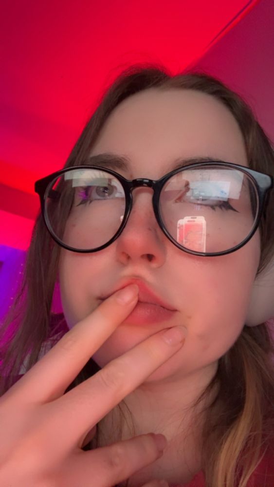 Scrunchie with big black glasses hand to her mouth with red lighting all around 