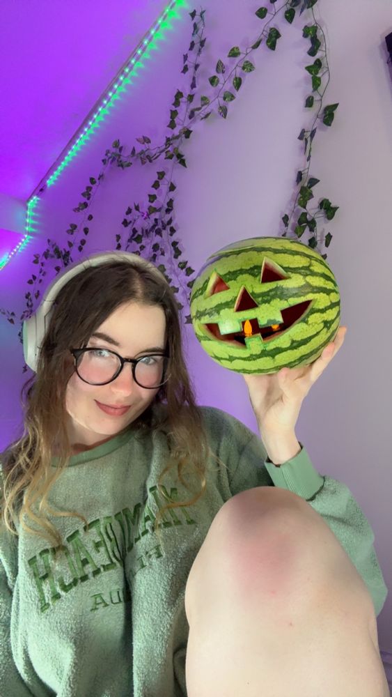Scrunchie holding a watermelon that’s been carved to look like a jack-o’-lantern 