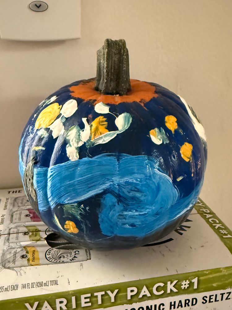 A pumpkin painted with Van Gogh’s Starry Night resting on a case of white claw variety pack