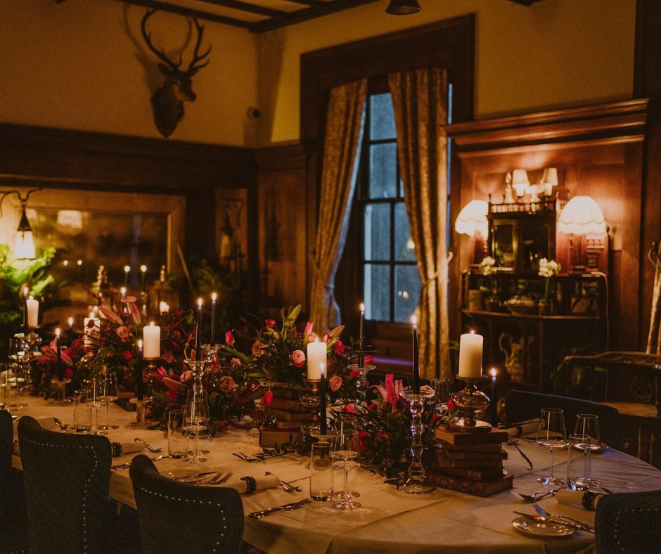 A dining room lit by candles and sconces with a beautiful tablescape laden with flowers.