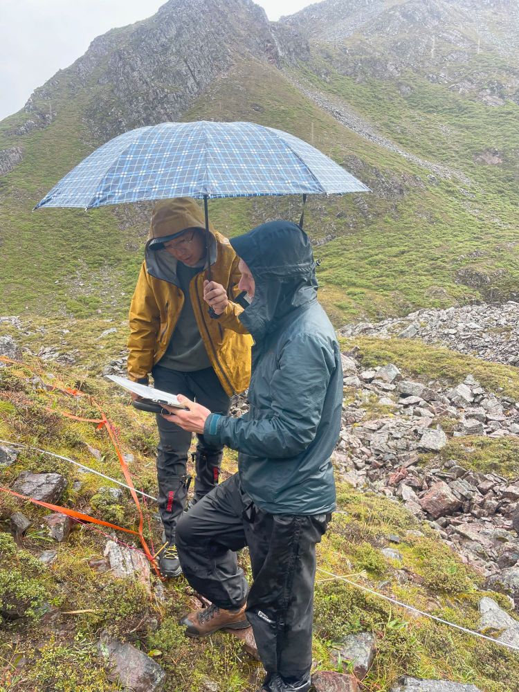 Fang Ye of Shangri La Alpine Botanical Garden and Robbie Hart of Missouri Botanical Garden work together to resurvey an alpine plant ecology monitoring plot in the rain. They’re both quite wet despite the umbrella Fang Ye is holding.