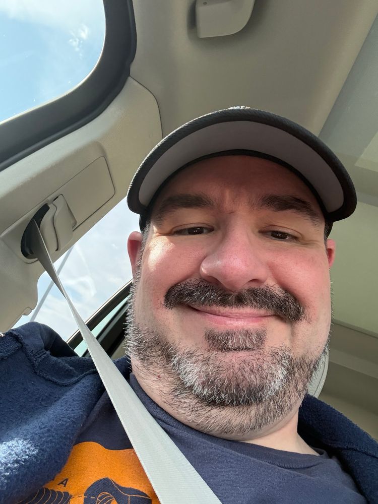 A photo of me in the car wearing a black cap and smirking. 