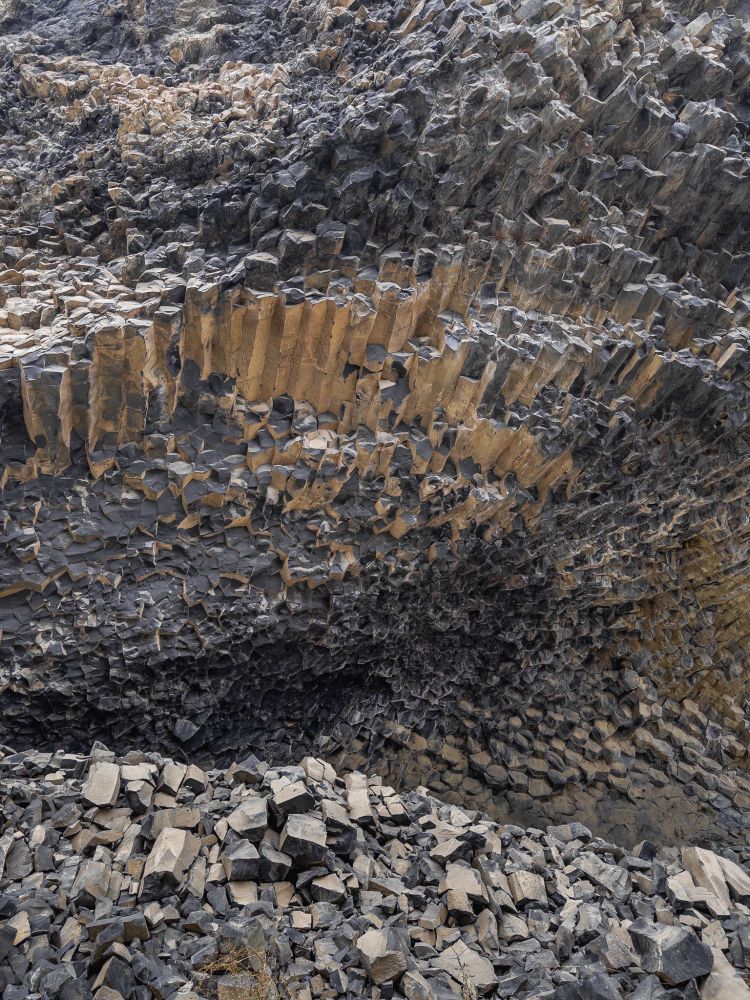 Another photo of basalt columns, this time in varying shapes and directions. View "leaning" over a small hill of rocks, overlooking a cave-ish formation