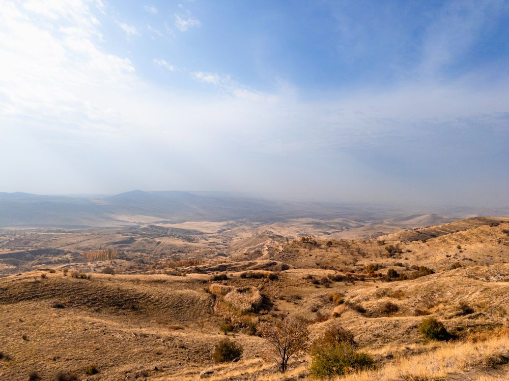 View of a vast range of barren hills, partly cloudy sky with a small patch of blue up close, cloudy and hazier hills on the horizon.