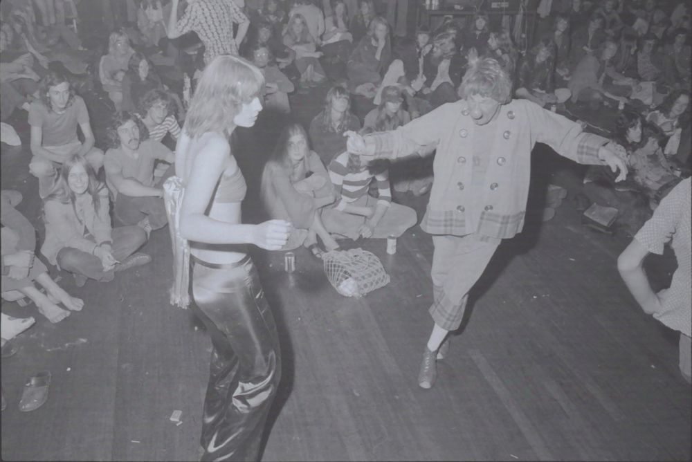 A clown and a young lady dance in front of a big group of young people at a gathering from the group Provadja. 