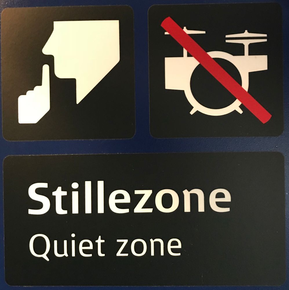 En skylt från ett danskt pendeltåg med texten Stillezone (quiet zone) och en piktogram på ett överstruket TRUMSET!!!
Också ett piktogram på en person som hyschar 