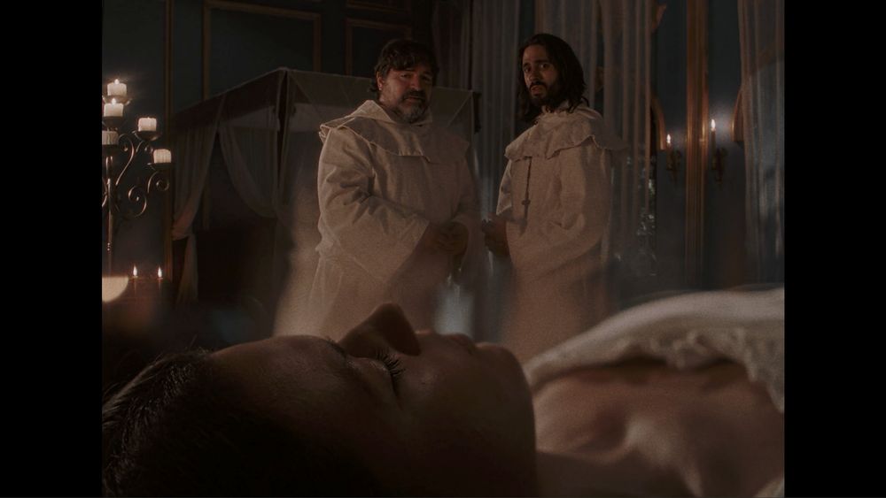 Two monks look concerned at a woman sleeping in the foreground.