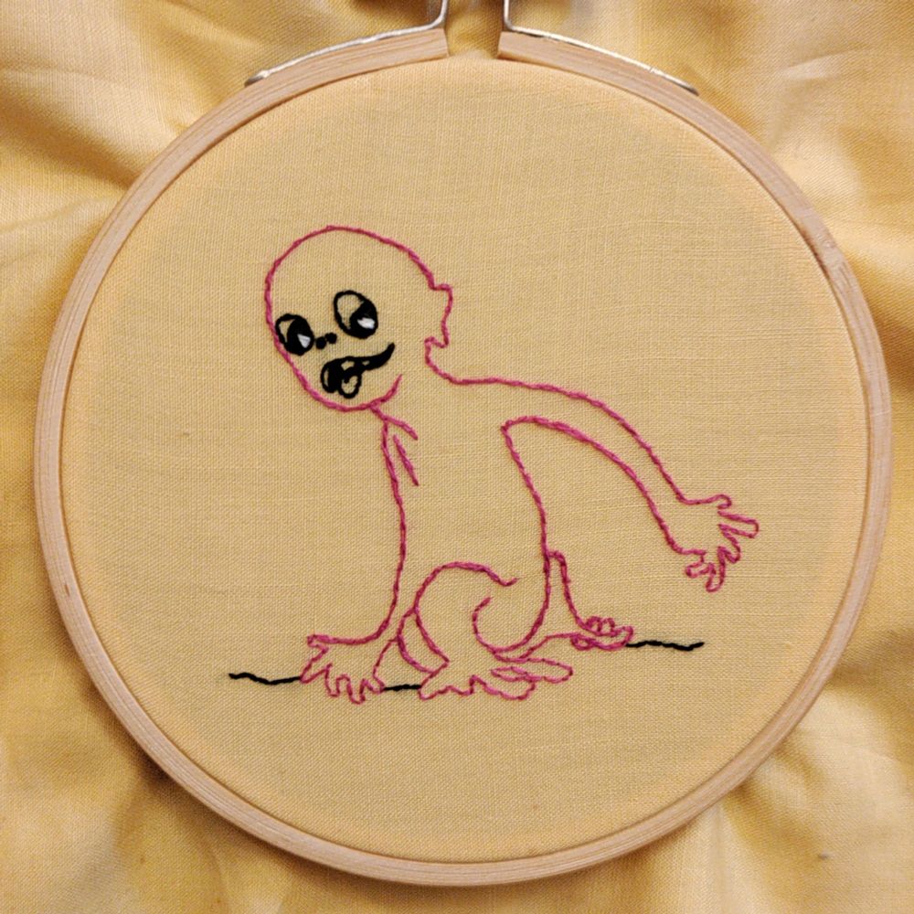 embroidery of a little goblin creature stitched in pink and black thread on yellow fabric, in a four-inch wooden hoop. he's sticking his tongue out and looks like he's sneaking away mischievously.
