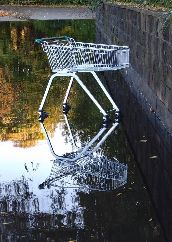 A lone shopping trolley casts an interesting reflection in a partly flooded supermarket car park