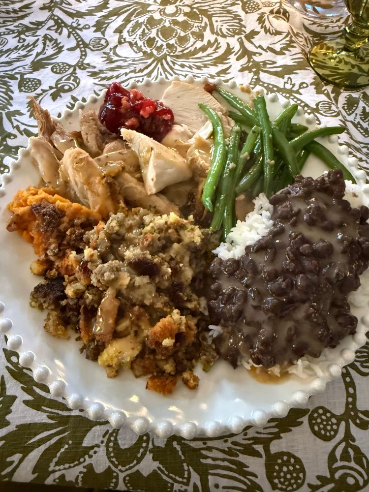 A plate loaded with turkey, cranberry sauce, stuffing, sweet potato, green beans, and black beans & rice 
