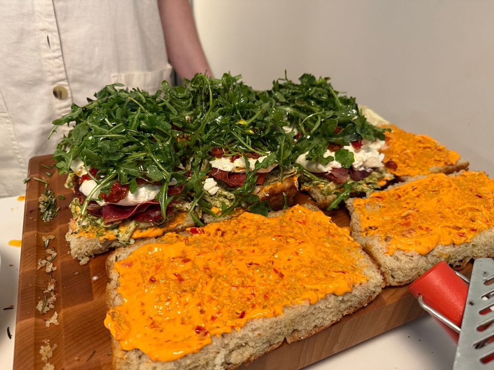 Sandwich assembly: homemade focaccia, Calabrian chili mayo, pesto chicken, crisped up pancetta and bresaola, burrata, sun dried tomato, and dressed arugula. 