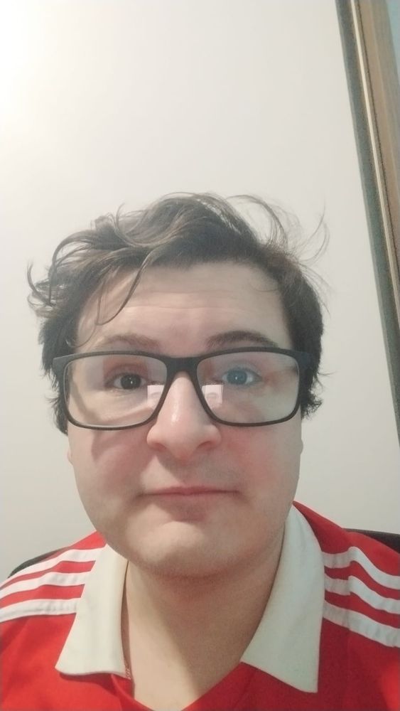 Selfie de uma pessoa com o cabelo curto, cor castanho escuro, usando óculos com uma armação preta