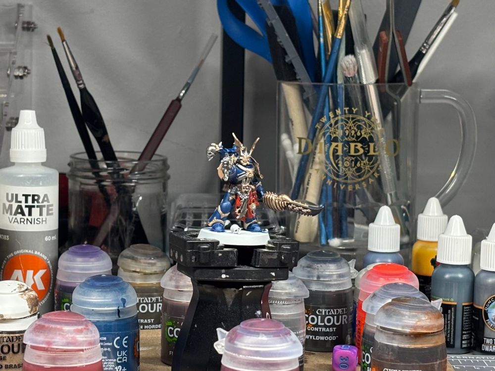 Close up of messy desk zoomed in on a night lord champion partially painted. Surrounded by various paints and brushes. 