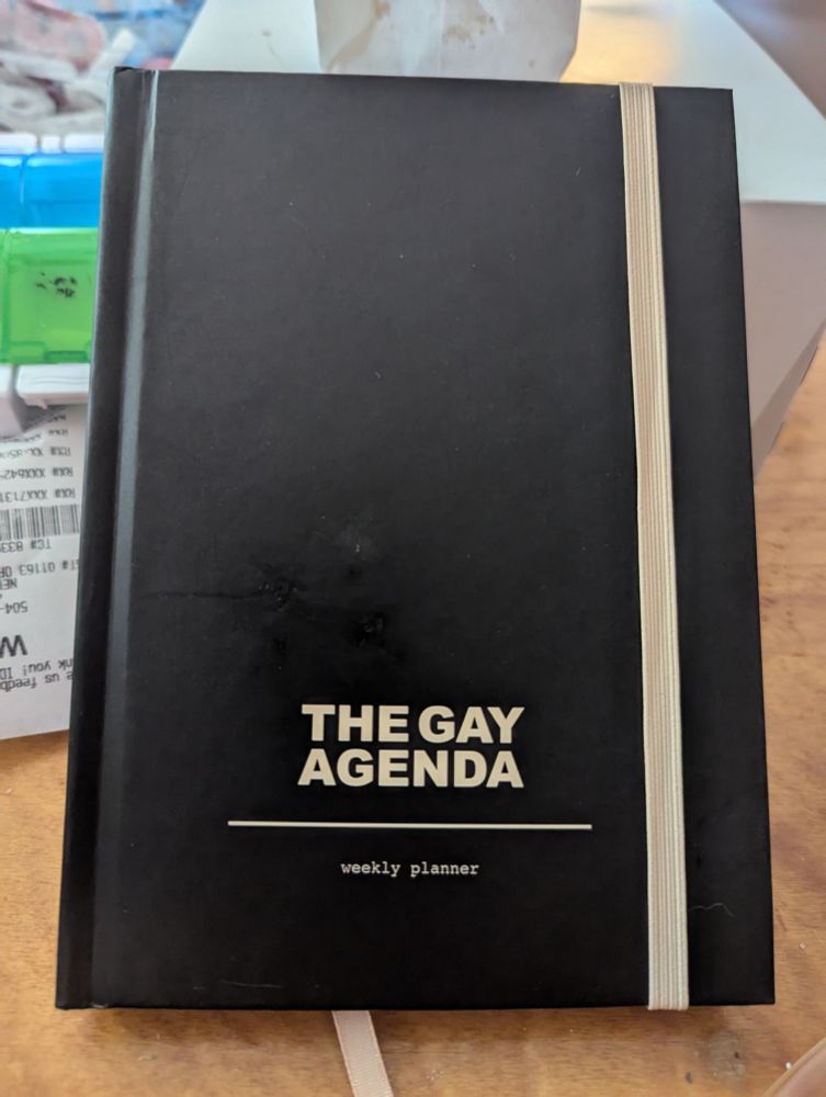 A black weekly planner with gold letters saying "The Gay Agenda"