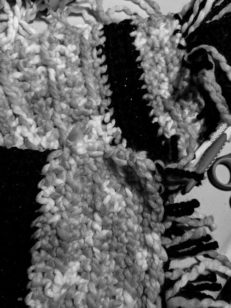 Grayscale image of a beginner crochet scarf with fringe with 2 crochet hooks off to the side