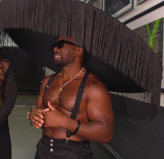 Xavier Woods wearing an enormous round black hat with tassels, roughly the size of Zelena Vega