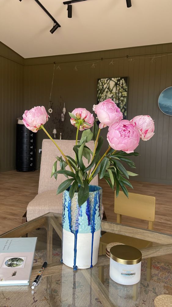 A vase with 5 stems of peony on a coffee table in an art studio. 