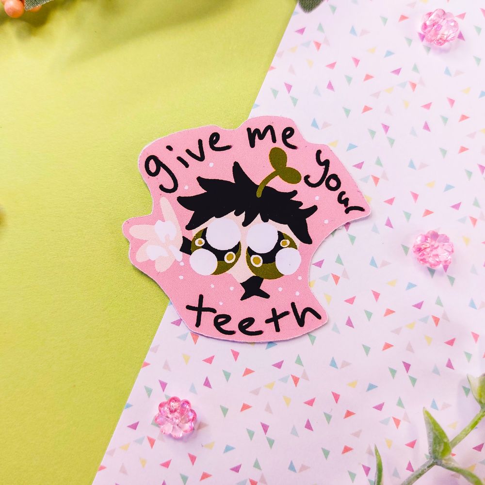 A sticker of a cartoon person looking up with very big sad eyes begging you to give it your teeth with a hand out holding teeth, on a light pink background surrounded by text saying "give me your teeth