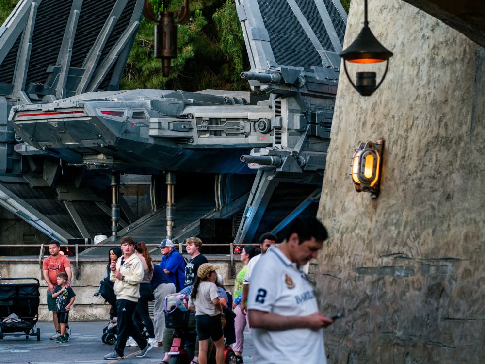 A First Order shuttle sits on a landing pad in the background as people pass by.